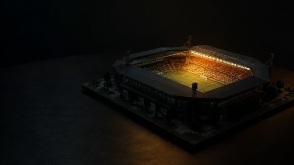 Pieni pienoismallistadion tummalla pöydällä, lämmin hehku vain kotikatsomon yllä, kotiedun tunnelma, kotietu lajeittain