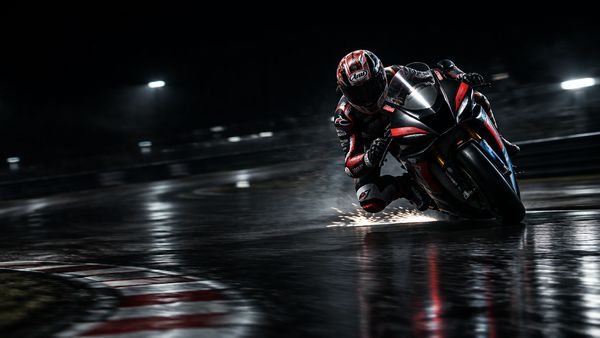 MotoGP-tyylinen kilpamoottoripyörä kallistuu kaarteeseen tummalla märällä radalla yöllä, kipinöitä, liike-epäterävyyttä. MotoGP