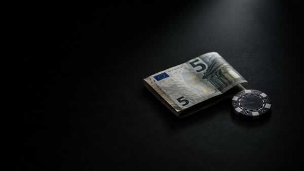 Taitettu viiden euron seteli ja yksi pelimerkki mustalla pöydällä kohdevalossa, 5 euron talletus kasinolle